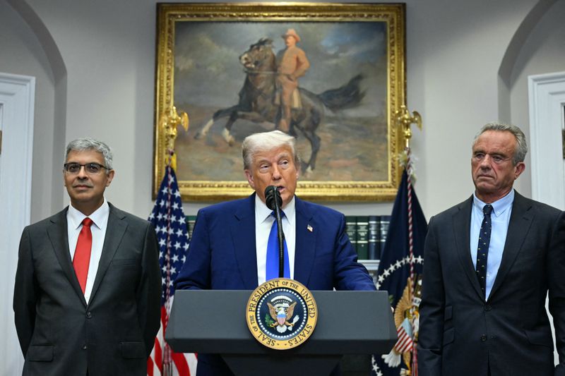 Jayanta Bhattacharya, Donald Trump and Robert F. Kennedy Jr. stand in front of a painting and a bookshelf in the Roosevelt Room of the White House. 