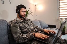 Soldier working on a laptop with headphones on while seated on a couch