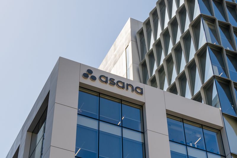 The Asana logo is seen on the side of a gray building with windows.