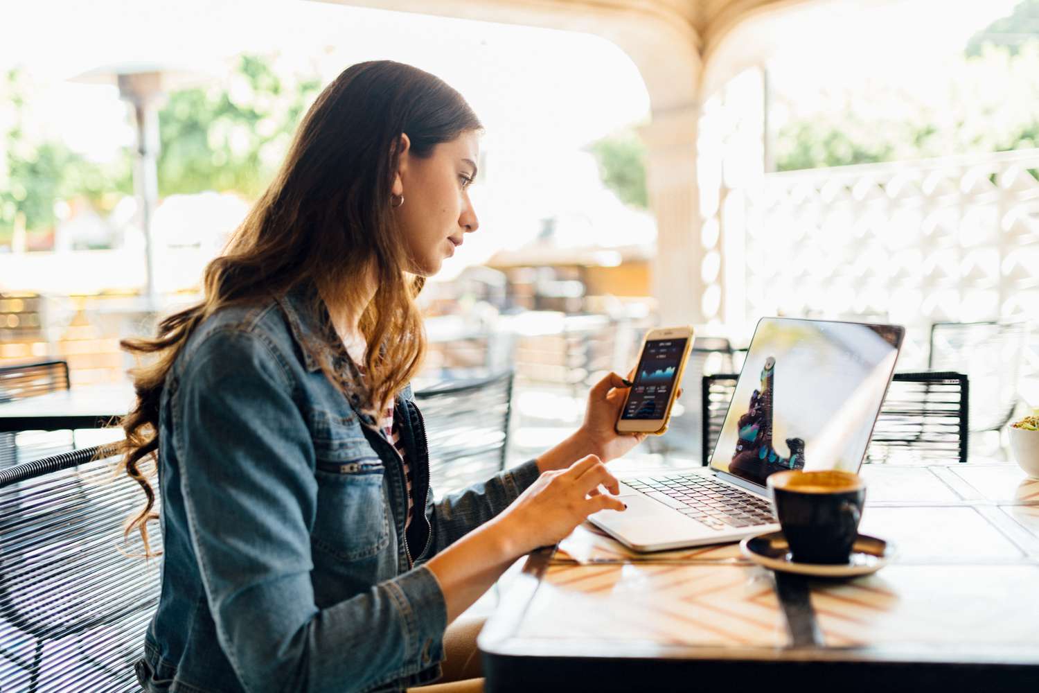 Image shows an investor using a laptop and a mobile phone to check up on investments while sitting at an outdoor cafe.