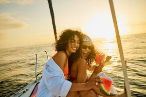 Two individuals on a boat at sunset holding watermelon slices, smiling and enjoying the moment