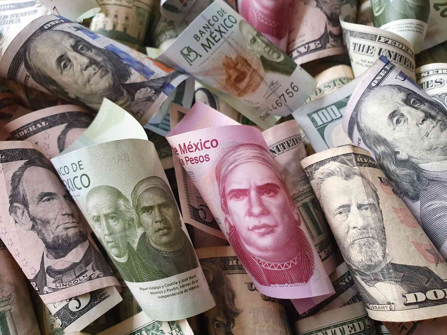 A close up of rolled up United States currency and Mexician Pesos spred on a surface