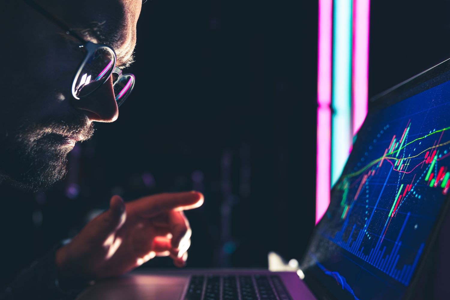 A trader leans in to read the price data displayed on a laptop screen showing trading bands on a stock chart.