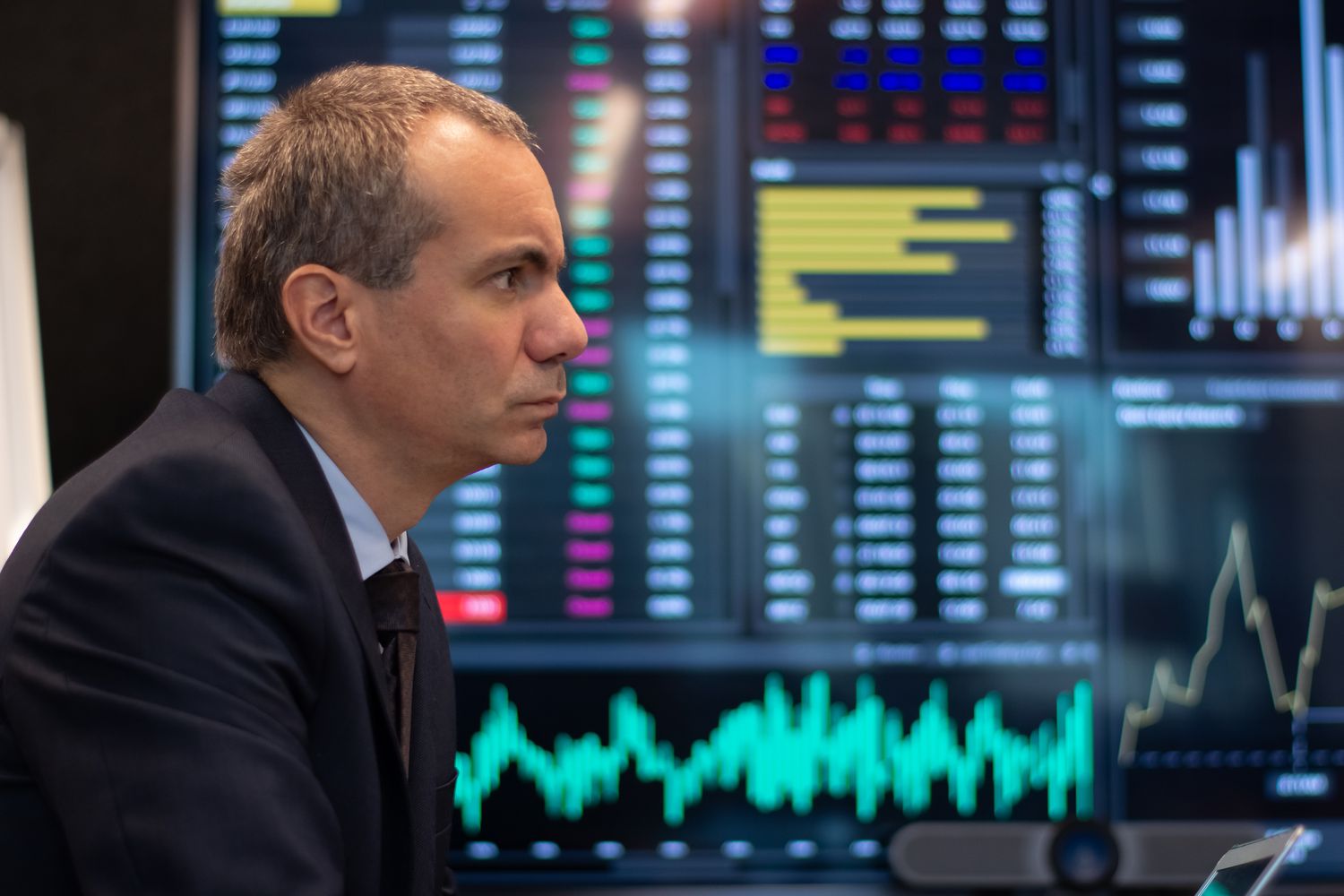 Side view of an investor focusing on digital screens displaying prices of stocks and market trends.