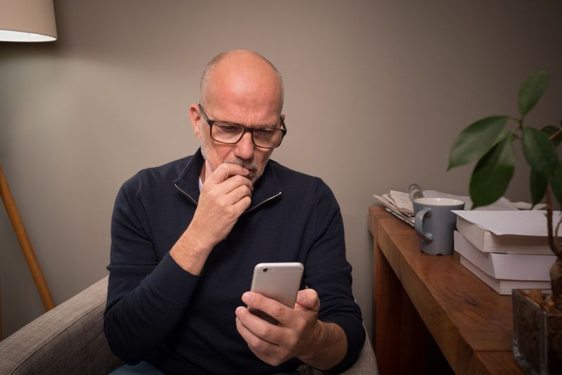 Mature man at home using smartphone for online banking, shopping, social media, e-mail, etc.