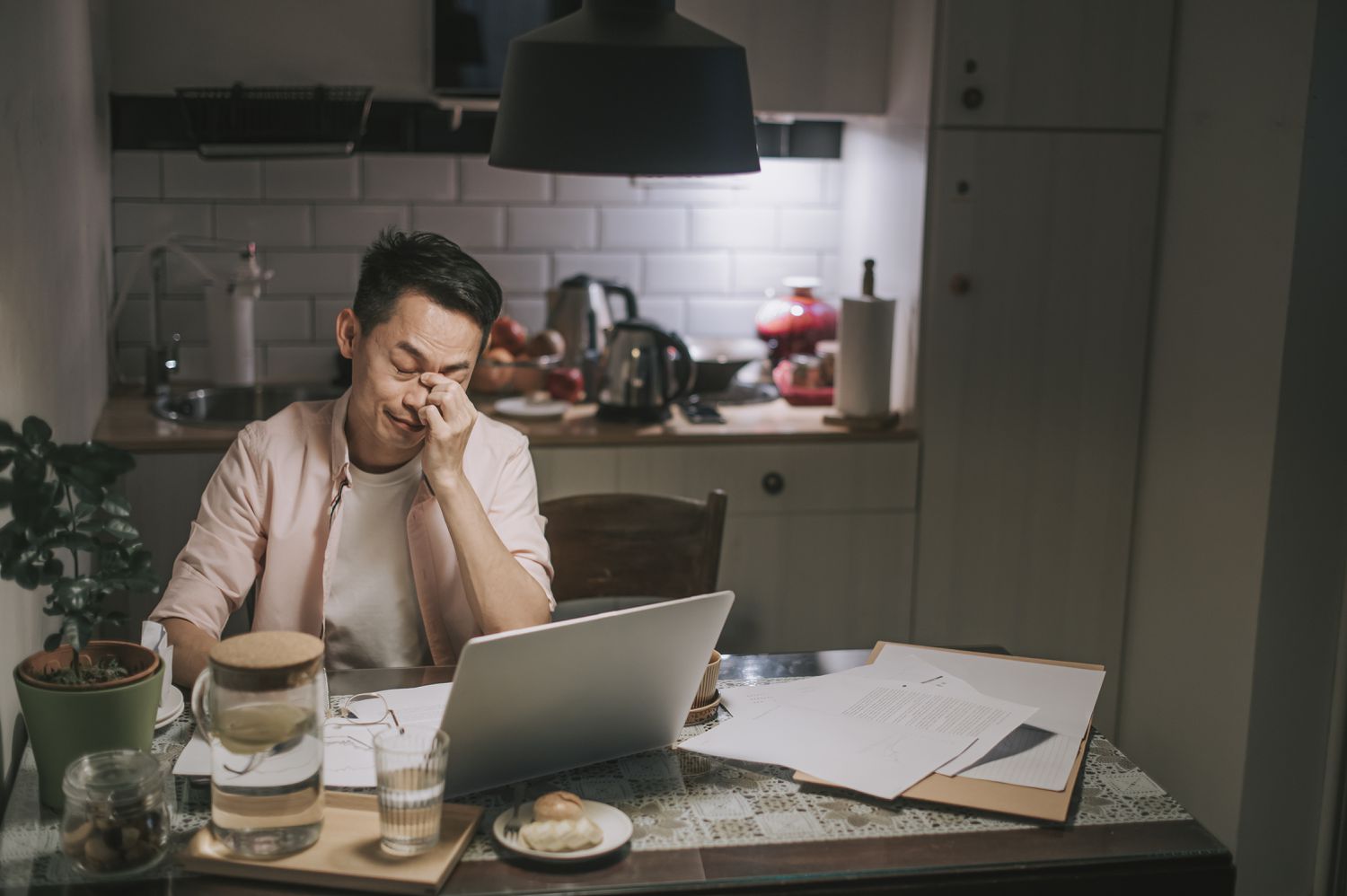 Asian male worries about his debt while sitting in the kitchen at night