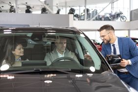 A couple selecting their new car at a car showroom while being shown around by a salesperson.