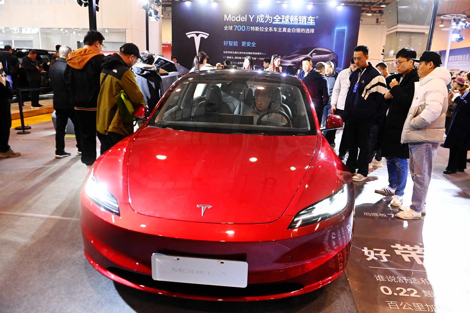 A group of people stand around a red Tesla vehicle on the floor of a car show in China.