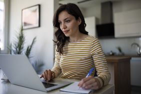 Young woman working at home with a laptop and notepad.