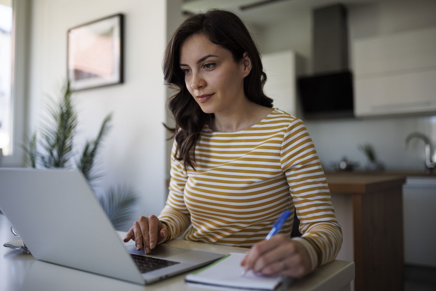 Young woman working at home with a laptop and notepad.