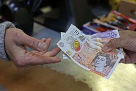 A close-up of two hands exchanging British pound notes as a shopkeeper passes a customer change.