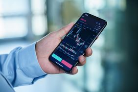 Man's hand holding a mobile phone which displays a stock chart.