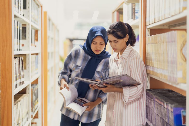 Two young students browsing for book inside a library.