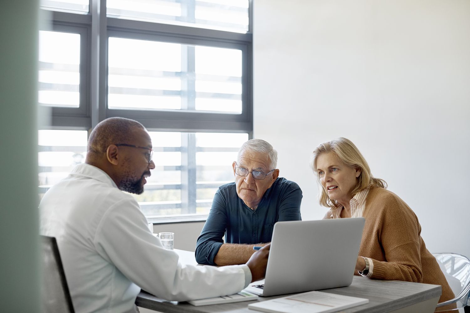 Man and woman sitting at a desk with a person pointing at a laptop screen