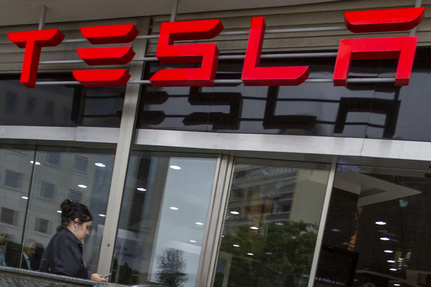 A person walks in front of a Tesla dealership in Lisbon, Portugal with a red TESLA sign overhead.