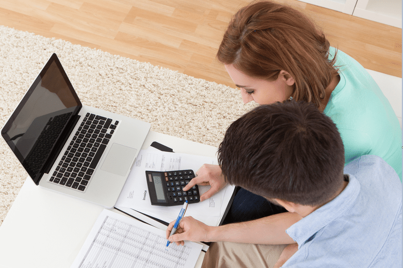 Seated couple at a low table go over finances together with a laptop and calculator. 