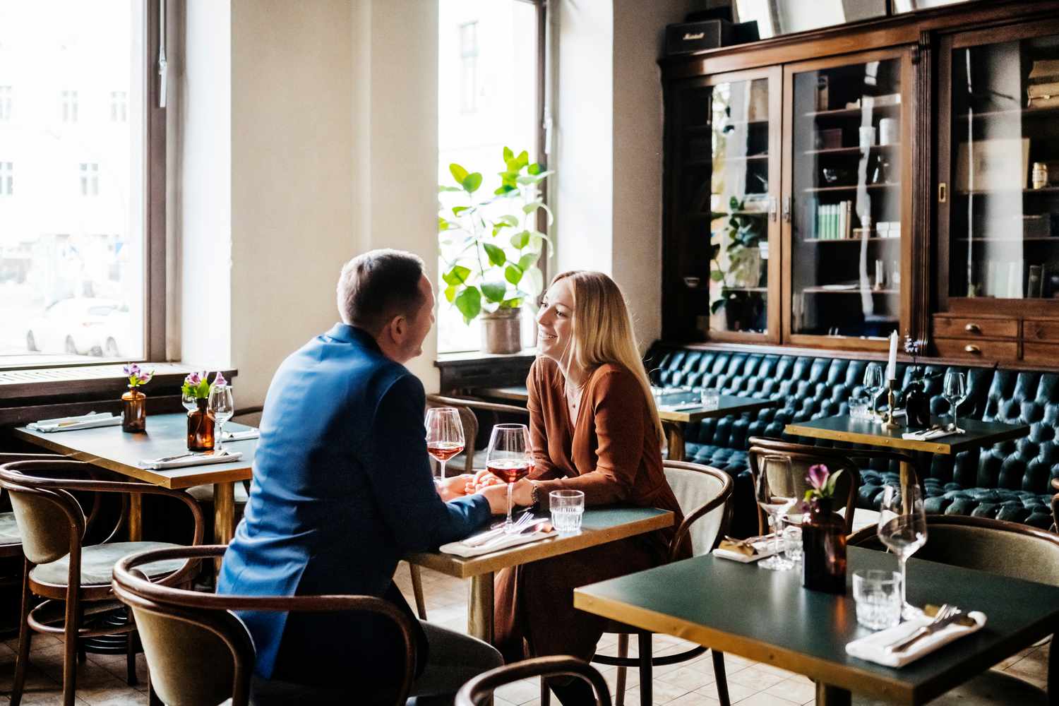 A couple holding hands while sitting down at a table and drinking red wine in a restaurant for lunch together,