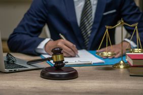 Businessperson in a suit with a gavel and mini-scale of justice nearby.