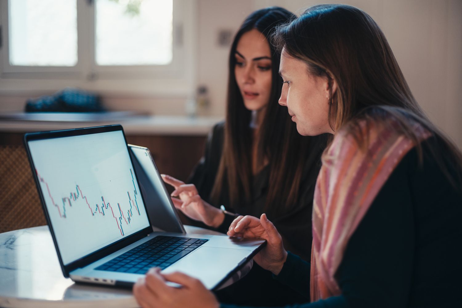 Two people having a discussion while in front of their laptops showing a digital chart of investment performance