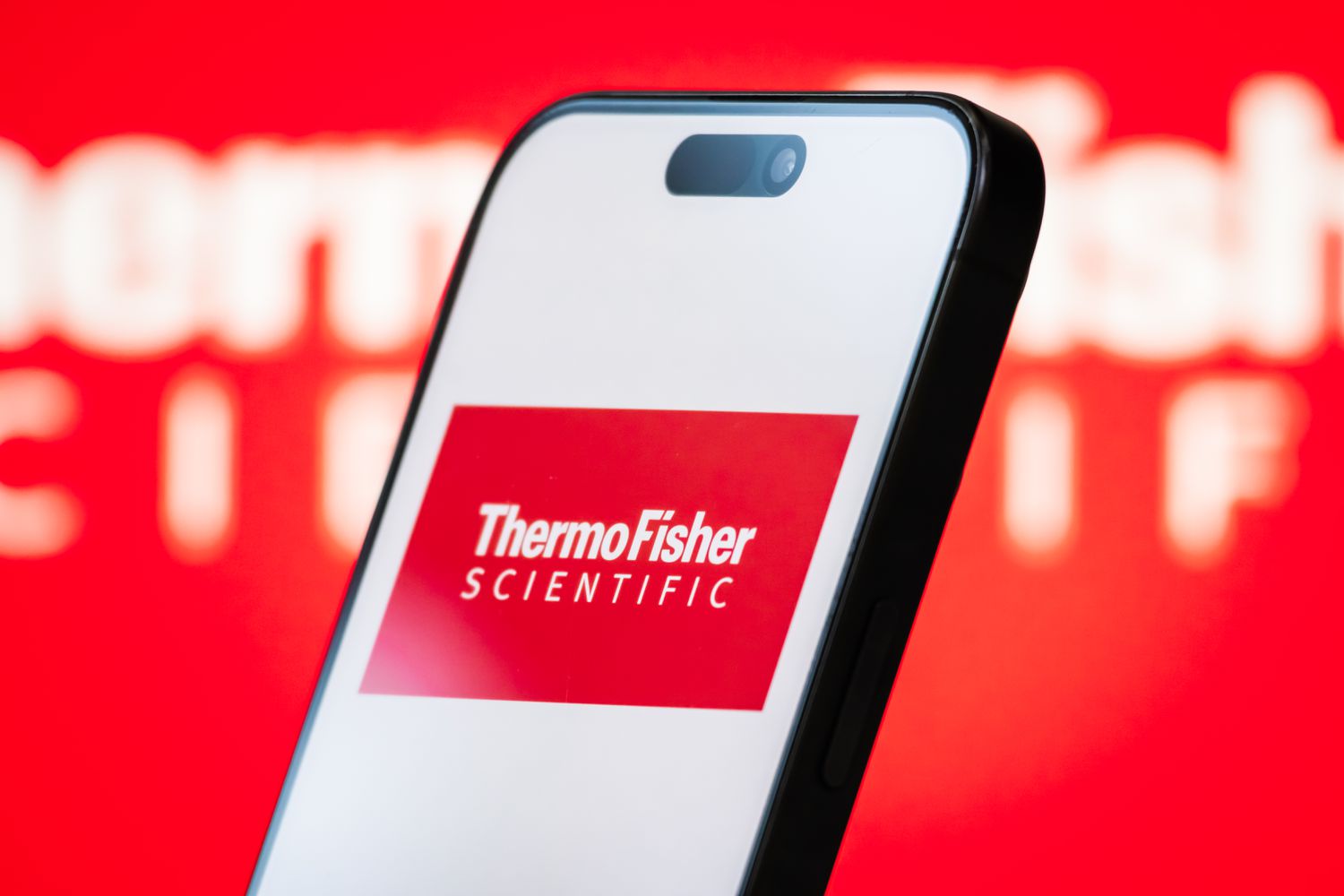 The logo of Thermo Fisher Scientific Inc. is displayed on a smartphone screen, with the company's branding in the background