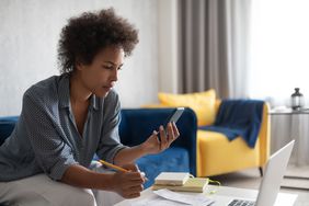Woman looking at a smartphone while working at a laptop