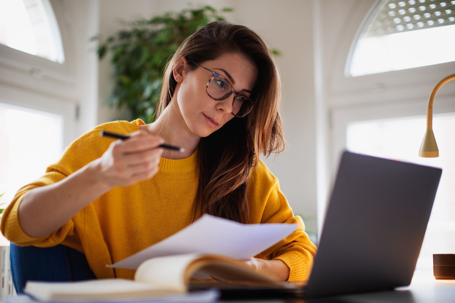 Young woman at home looking seriously at a laptop and a financial document