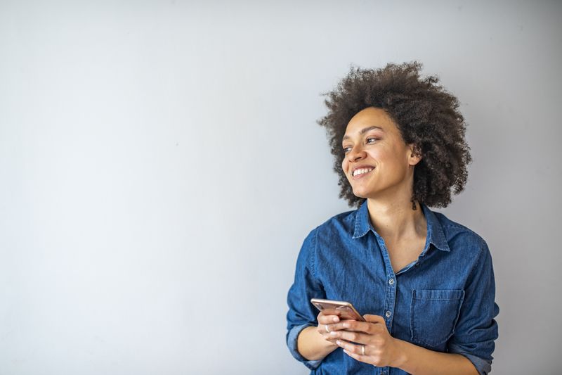 Smiling mature woman using smartphone isolated on gray wall with copy space. 