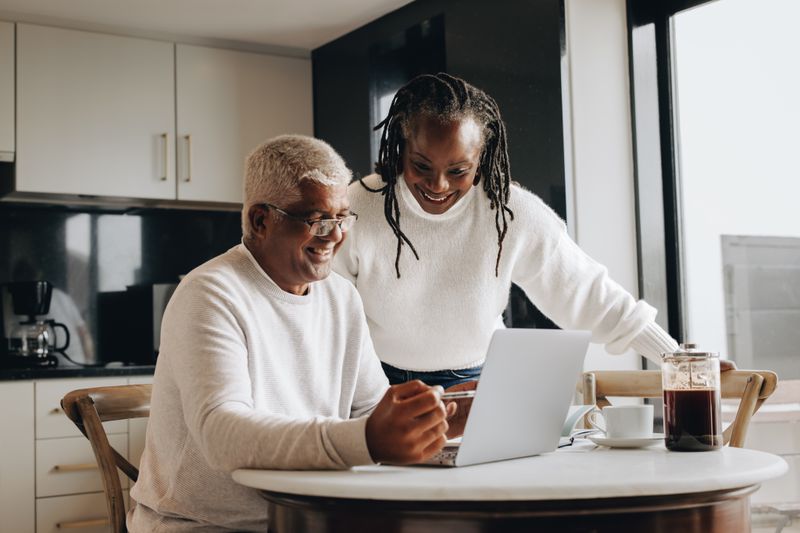 Older couple sitting in their kitchen and looking happily at mortgage rates on a laptop