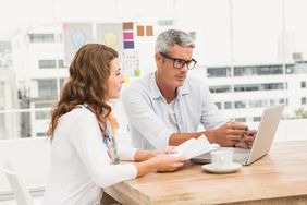 Couple in their 40s or 50s sitting in their kitchen and looking at mortgage documents and rates on a laptop