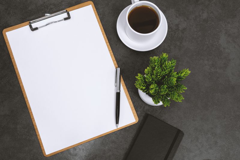Clipboard With Blank White Paper on Black Background With Coffee Cup and Notebook.