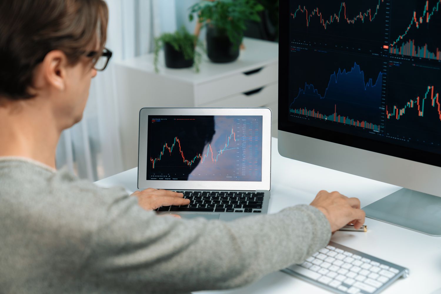 Person sitting at a desk with a large screen behind a laptop, both are displaying charts. 