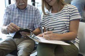 Close-up of a daughter helping her senior father fill out insurance paperwork in a clinic waiting room
