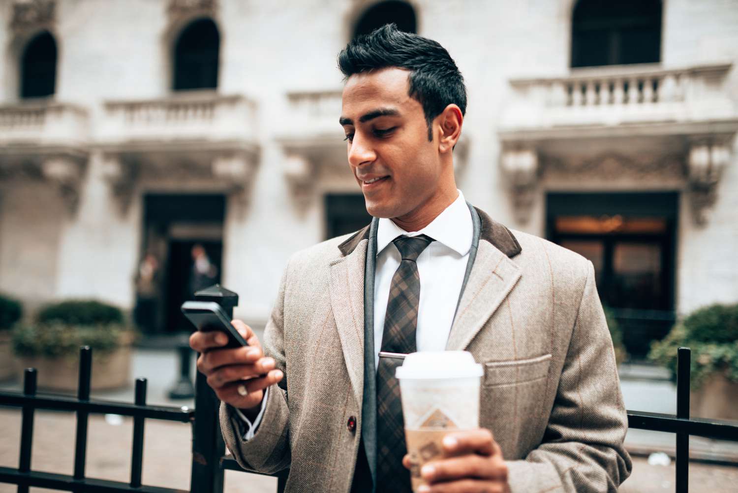 Man holding coffee cup and looking at his phone while on the street. 