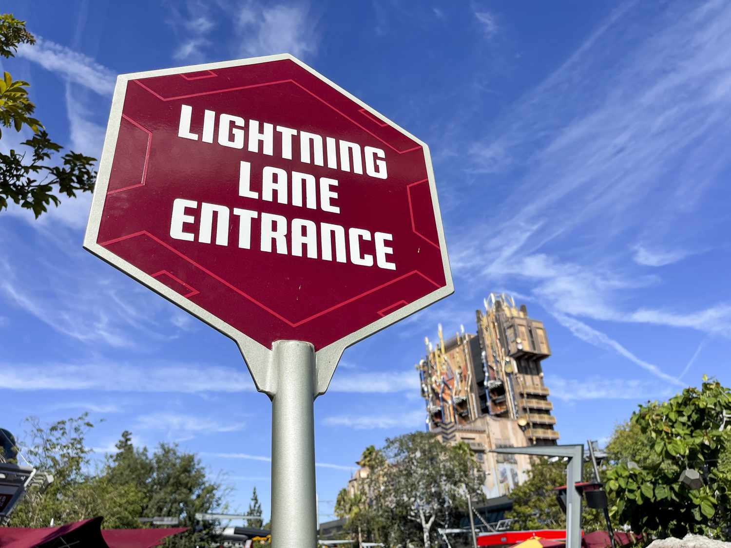 A red sign with the words "Lightning Lane Entrance" at a Disney theme park is seen in front of a blue sky