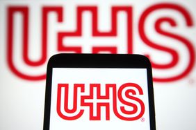 The red Universal Health Services logo is seen on a smartphone screen, with a larger version in the background.