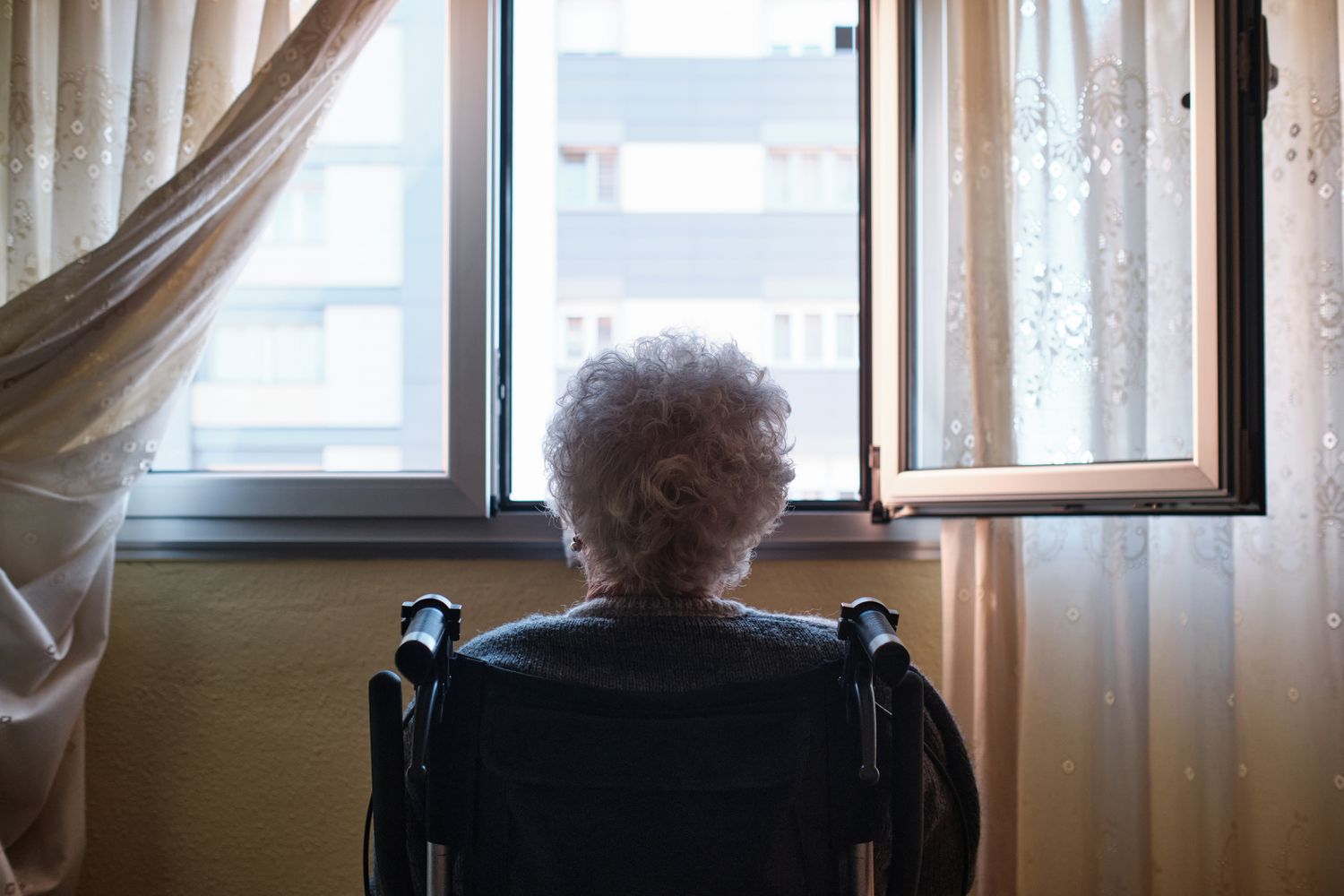 An older person looks out a window