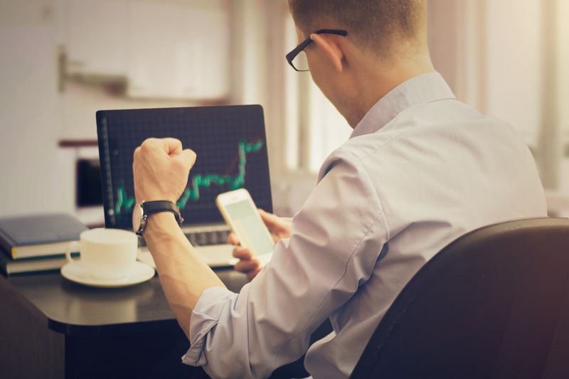 Rear View Of Cheerful Stock Broker With Fist Sitting In Office