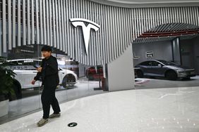 A person walks outside a Tesla showroom, with the company's logo next to the entrance.