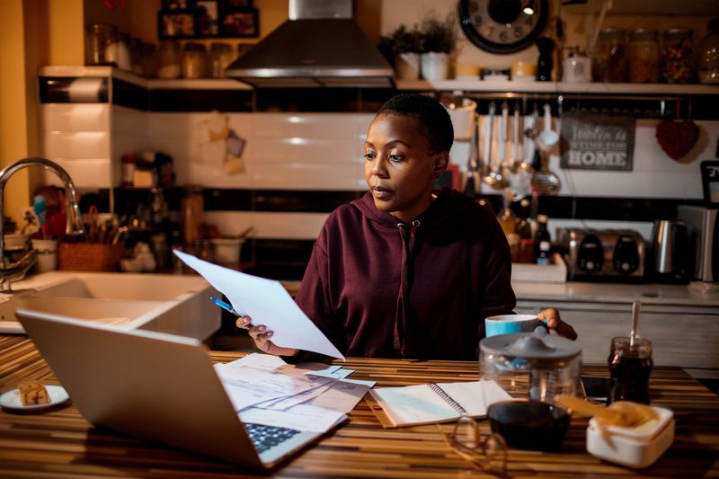 Person doing tax paperwork on a laptop at the kitchen counter 