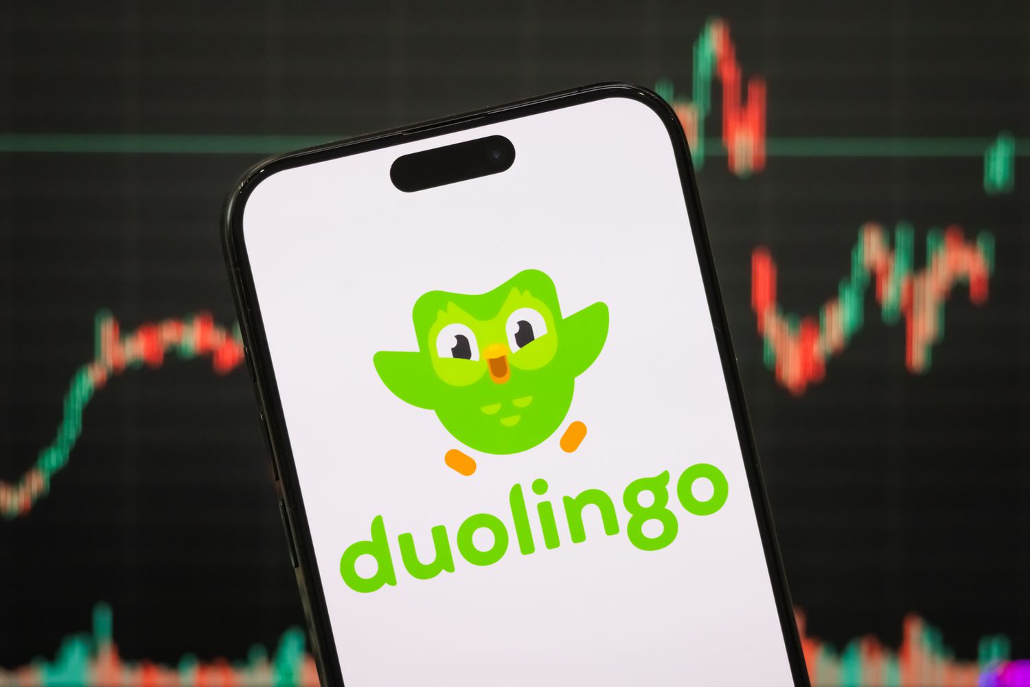 The Duolingo logo is seen on a phone screen, with the company's stock chart in the background.