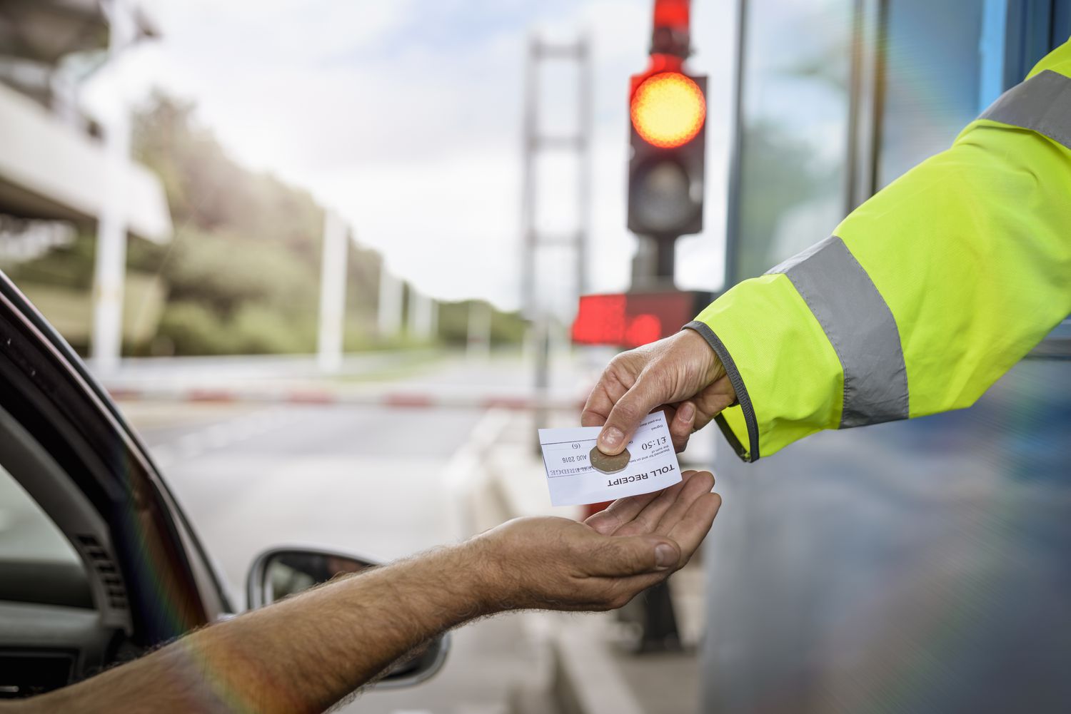 A toll road user in the United Kingdom receives change and a receipt from a booth operator after paying the user fee for the roadway.