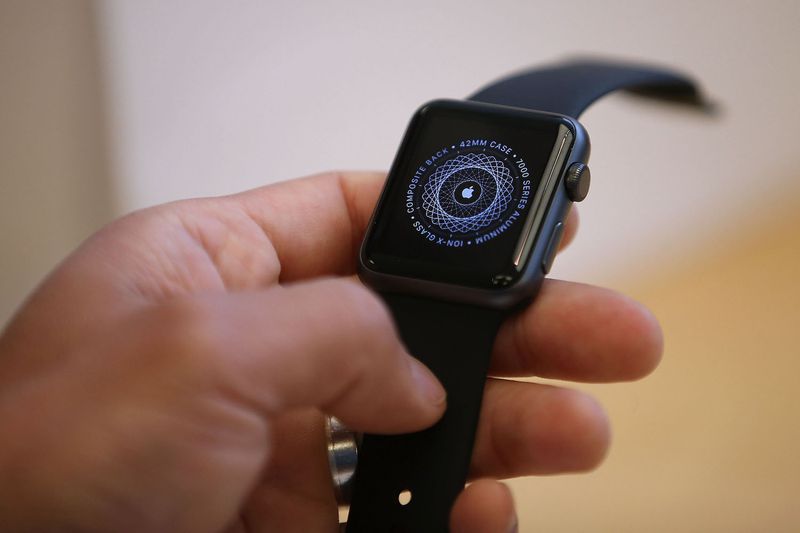 A hand holding an Apple Watch with the startup graphic on the screen.