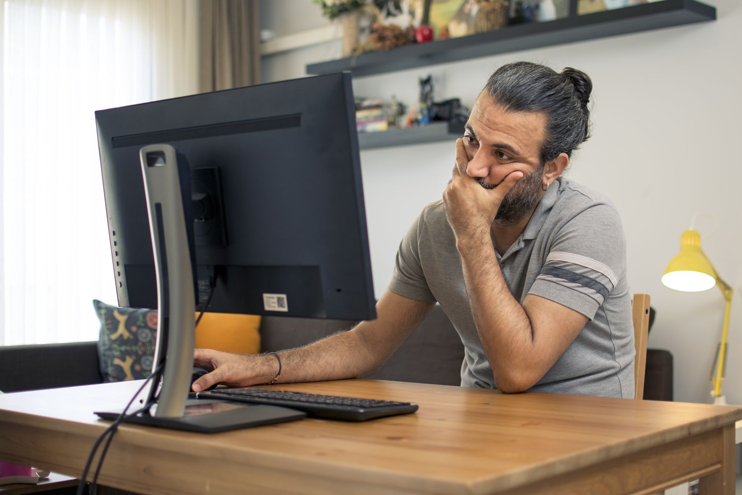 Man sitting at a desk looking at a monitor with his hand clenched over his mouth.