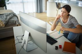 Closeup side view of an early 30's woman taking an online learning course. She's seated at a desk in her bedroom.