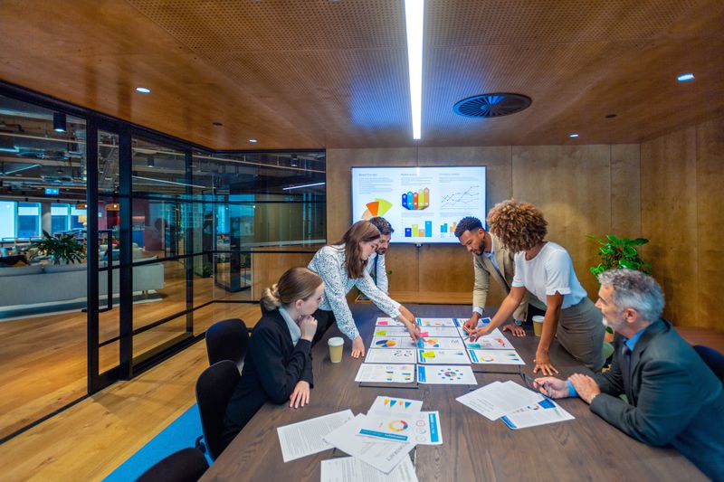 Fund managers gather around a conference table covered in documents and discuss how to invest in other mutual funds.