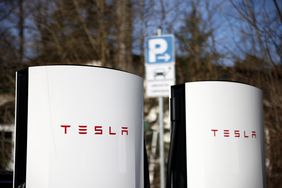 The red Tesla logo is seen on a pair of white Tesla charging stations.