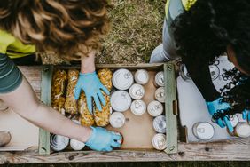 Two people, pictured from above, organize cans and packages of food in donation boxes.