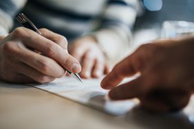 Cropped hands signing a piece of paper with another hand pointing at where to sign