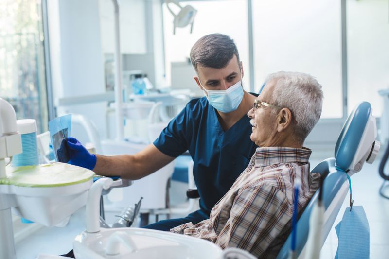 A man sits in a dentist chair looking at an x-ray with the dentist