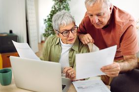 Older couple at home, looking at financial documents and a laptop
